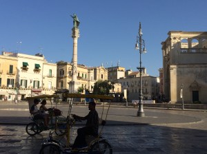 The central square dominated by the statue of a former Pope and the Roman amphitheater beneath it.